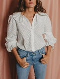 Woman wearing a white patterned blouse and blue jeans against a pink background