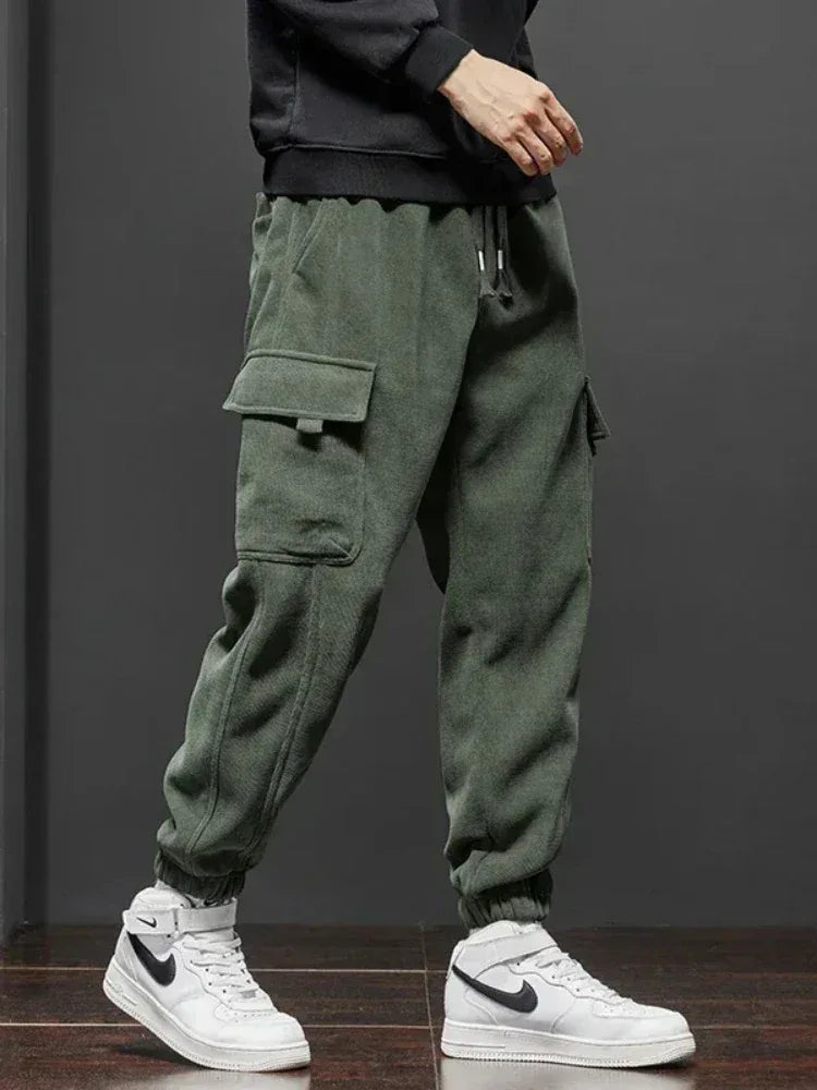 Person wearing green cargo pants and white sneakers with a black logo on a dark background