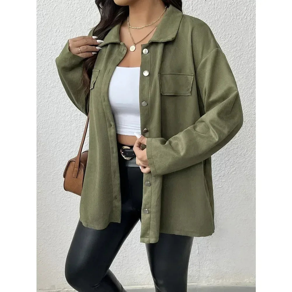 Person wearing an olive green jacket over a white top and black pants, holding a brown handbag against a white background.