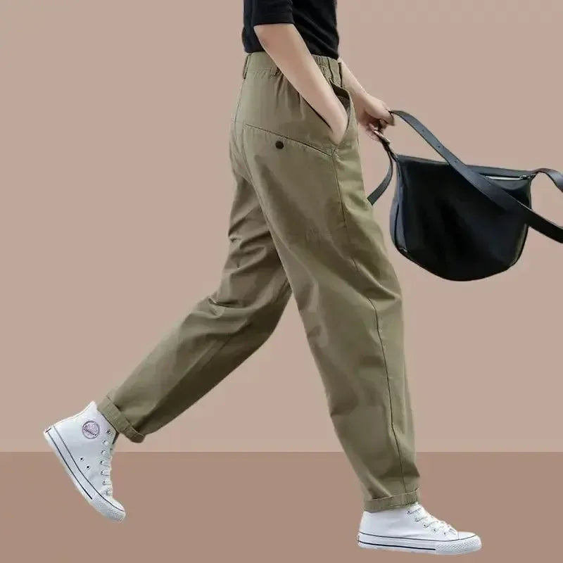 Person wearing khaki pants and white sneakers holding a black bag on a beige background