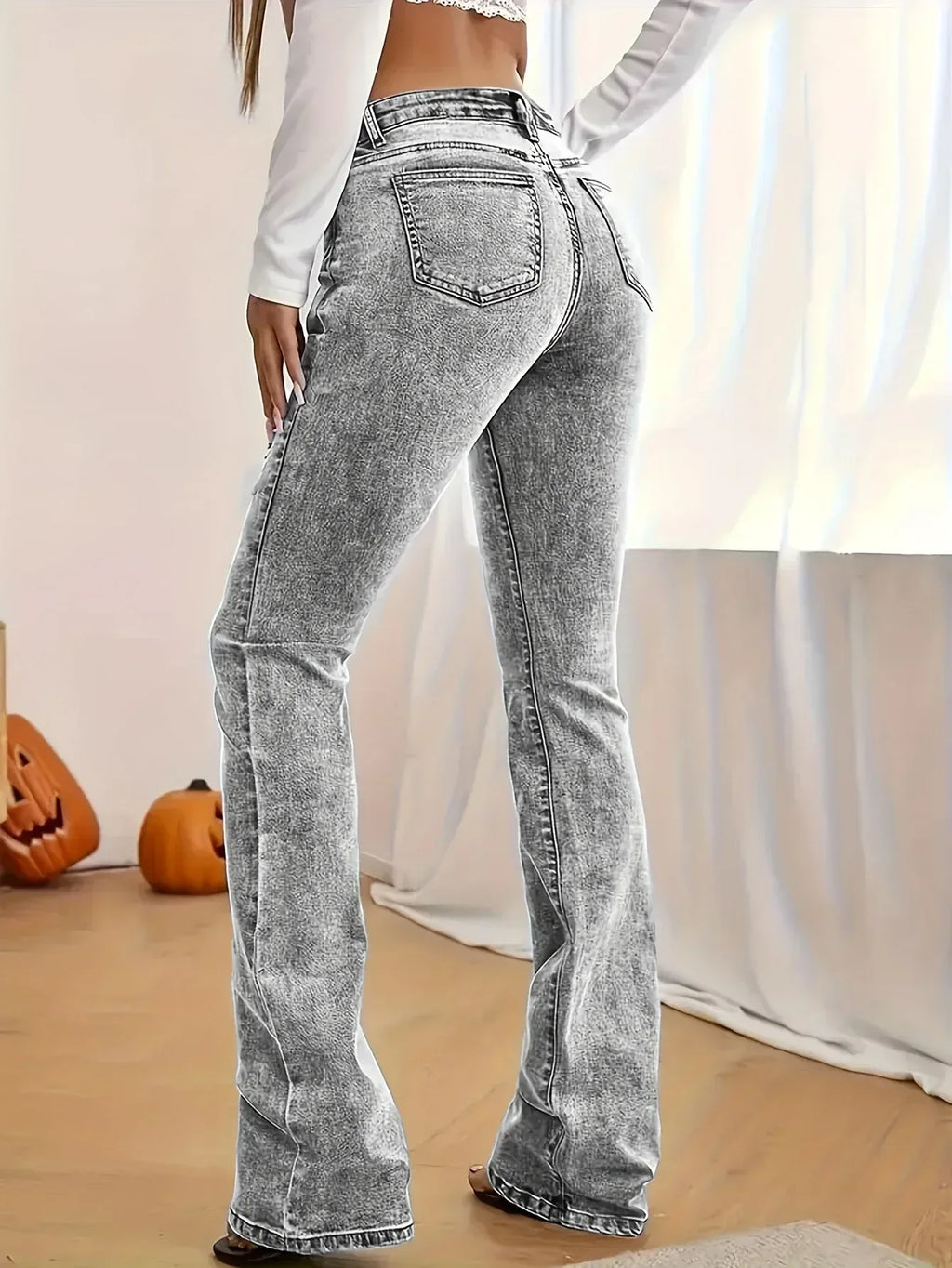 Person wearing acid-wash jeans in a room with pumpkins and a curtain.
