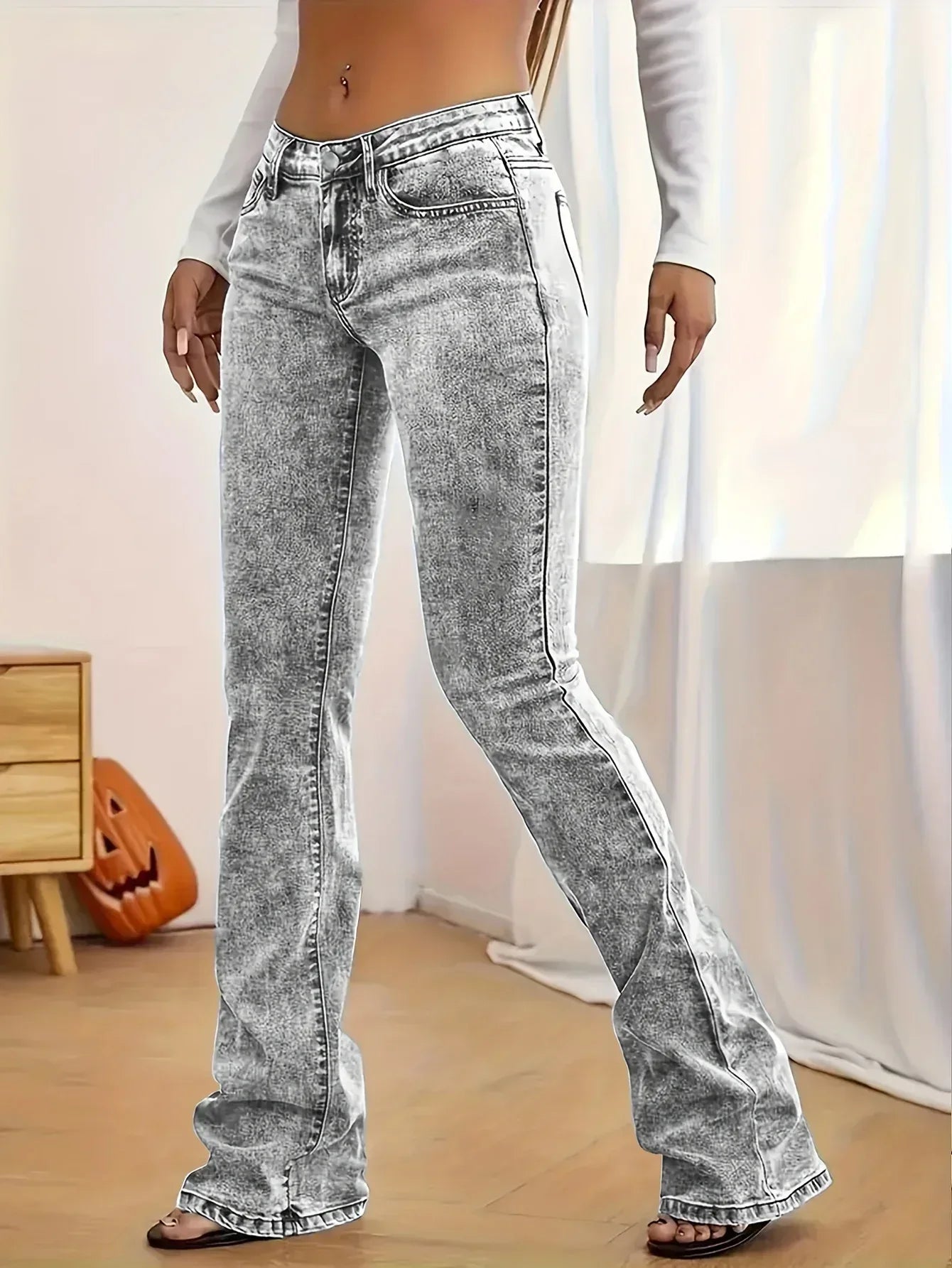 Person wearing acid-wash jeans in a room with a wooden floor and white curtain.