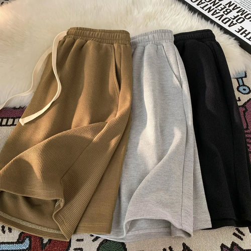 Three pairs of textured pants in brown, gray, and black on a patterned surface.