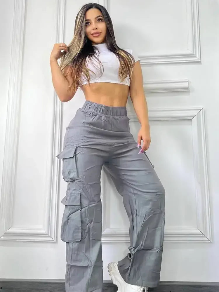Woman wearing a white crop top and gray cargo pants against a white paneled wall.