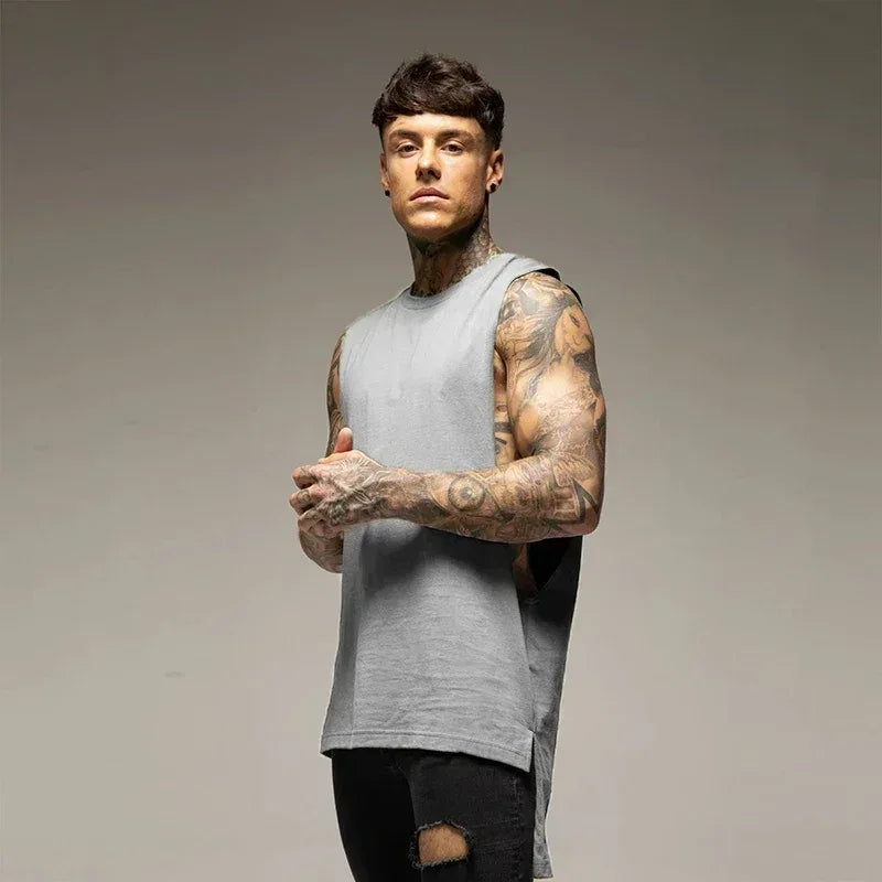 Man with tattoos wearing a gray sleeveless shirt against a gray background