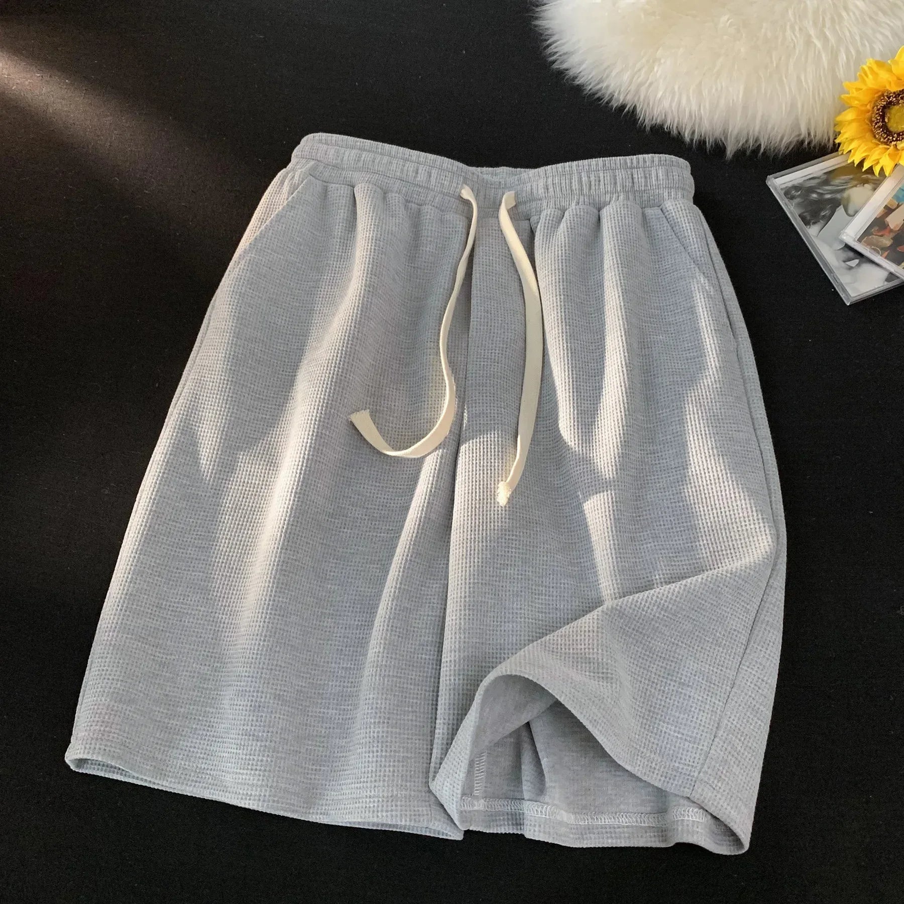 Light grey shorts with a drawstring on a dark surface.