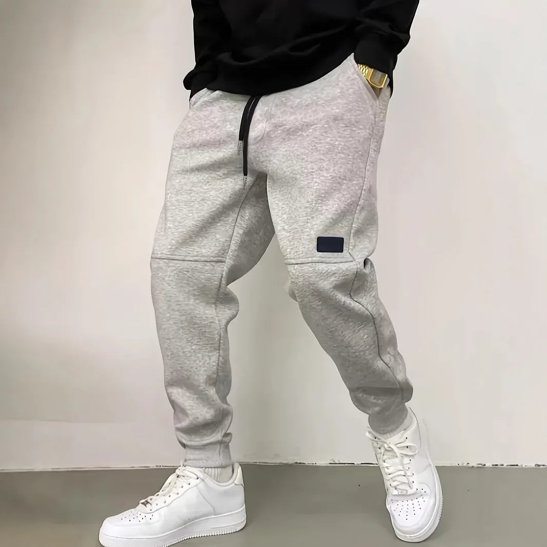 Person wearing gray jogger pants and white sneakers against a plain background