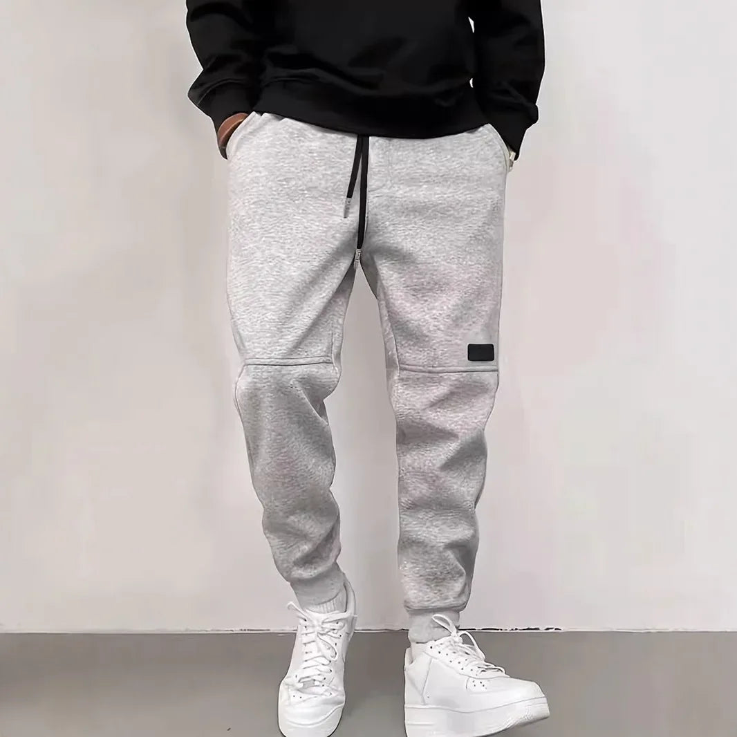 Person wearing gray jogger pants and white sneakers against a plain background