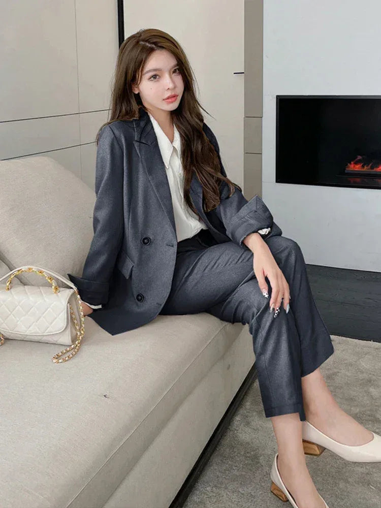 Woman in a gray suit sitting on a couch in a modern living room.