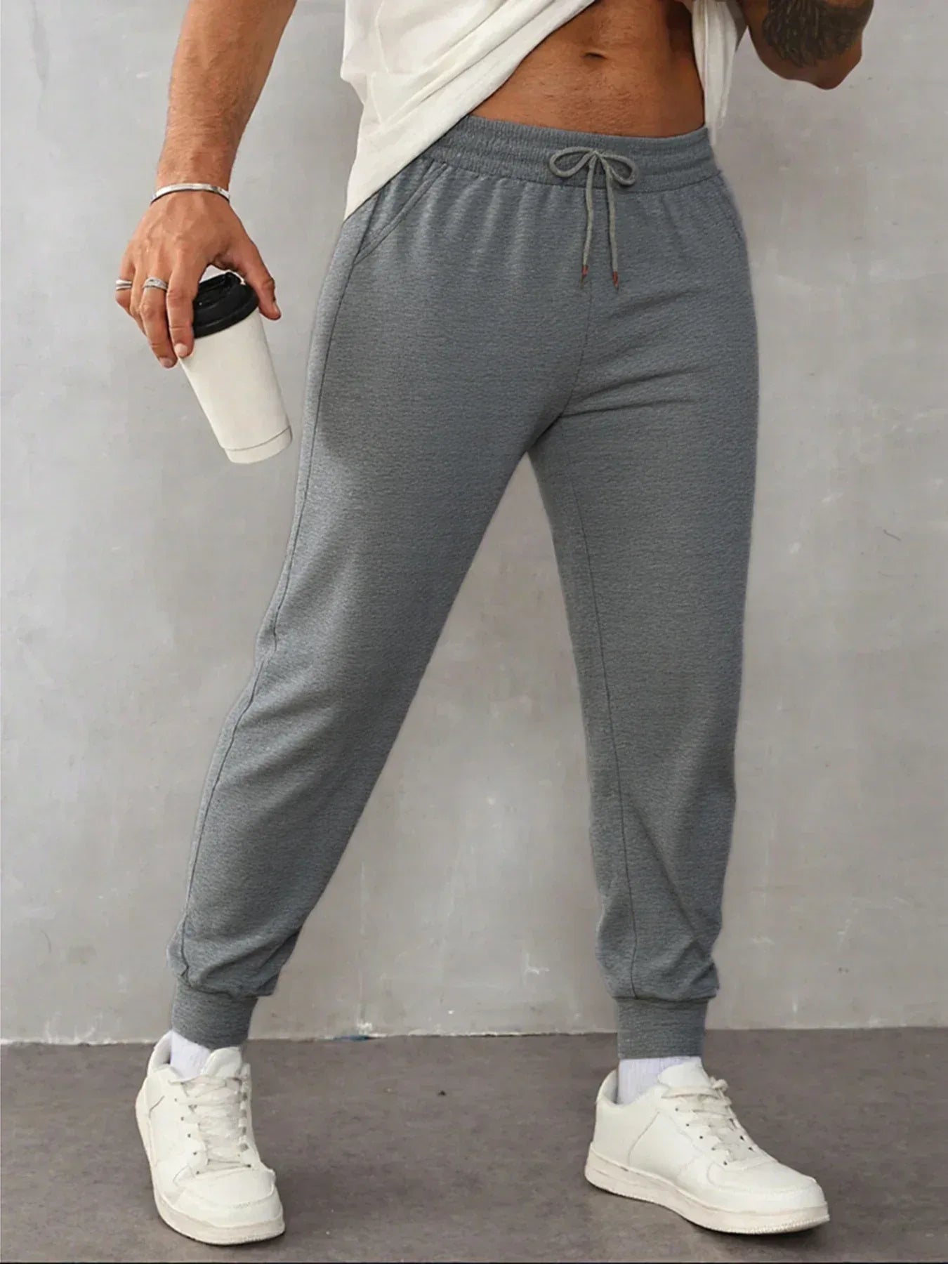 Person wearing gray sweatpants and white sneakers against a plain background