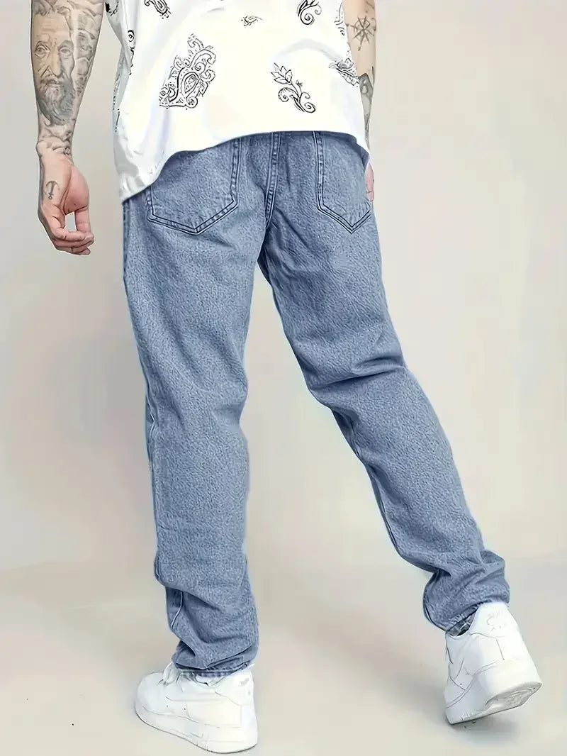 Person wearing light blue jeans and a white shirt with patterns on a plain background