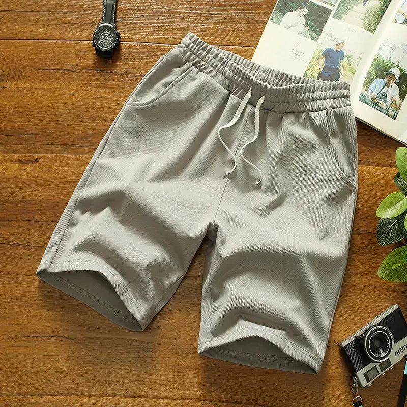 Light gray shorts on a wooden surface with a watch and photos in the background