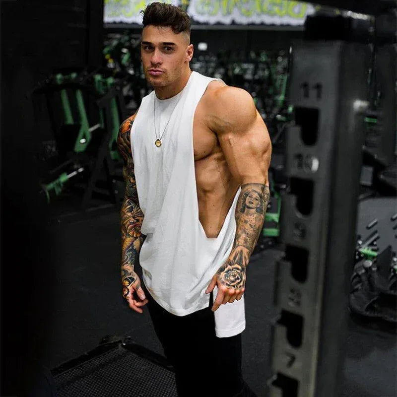 Muscular man with tattoos wearing a white tank top in a gym setting
