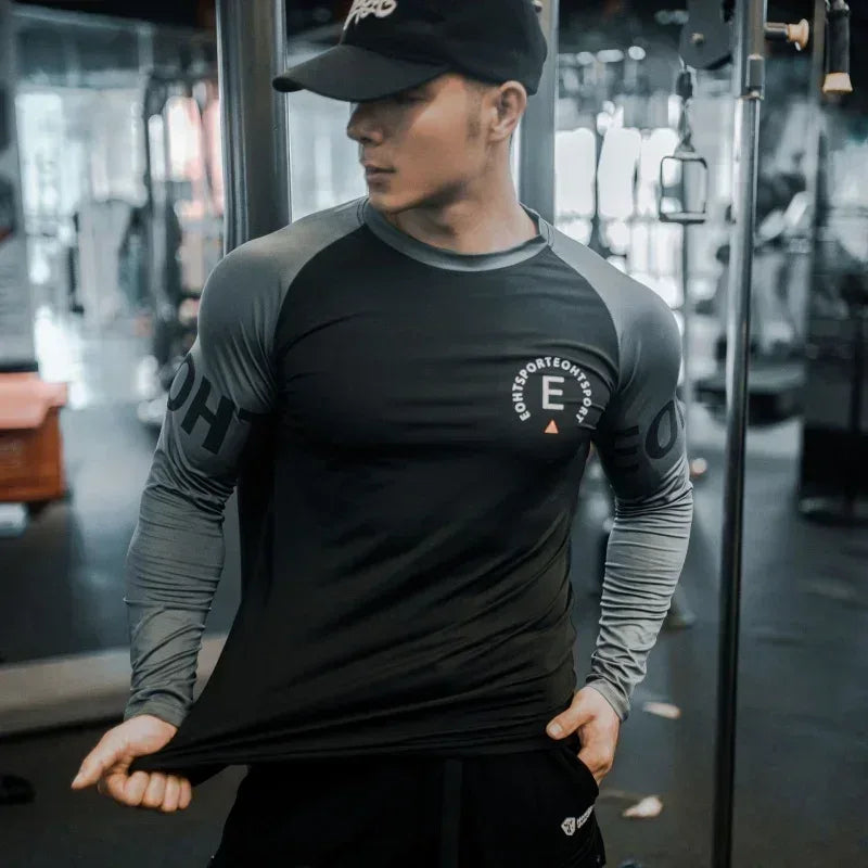 Person wearing a black and gray athletic shirt with branding in a gym setting