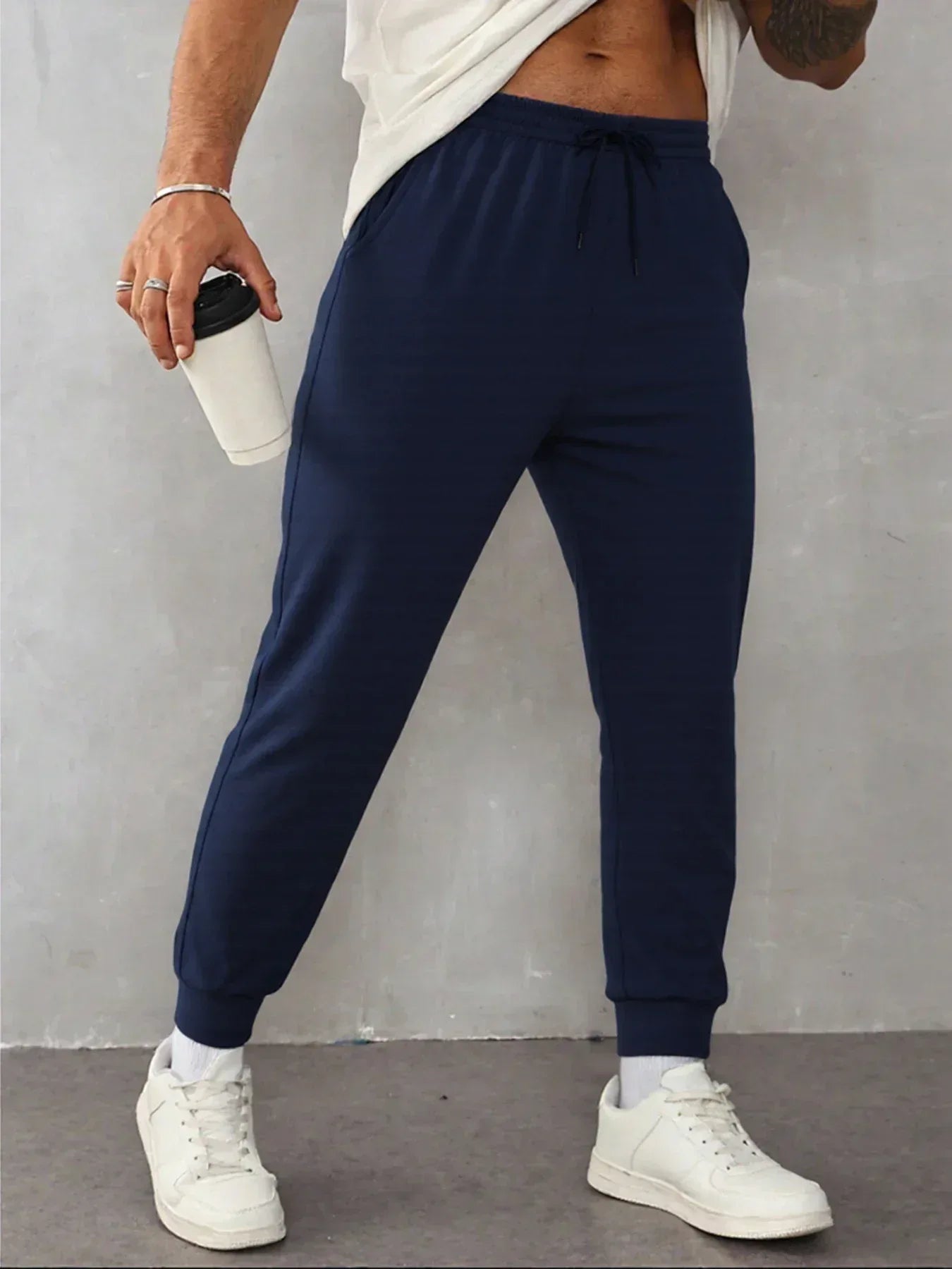 Person wearing navy jogger pants and white sneakers against a gray background