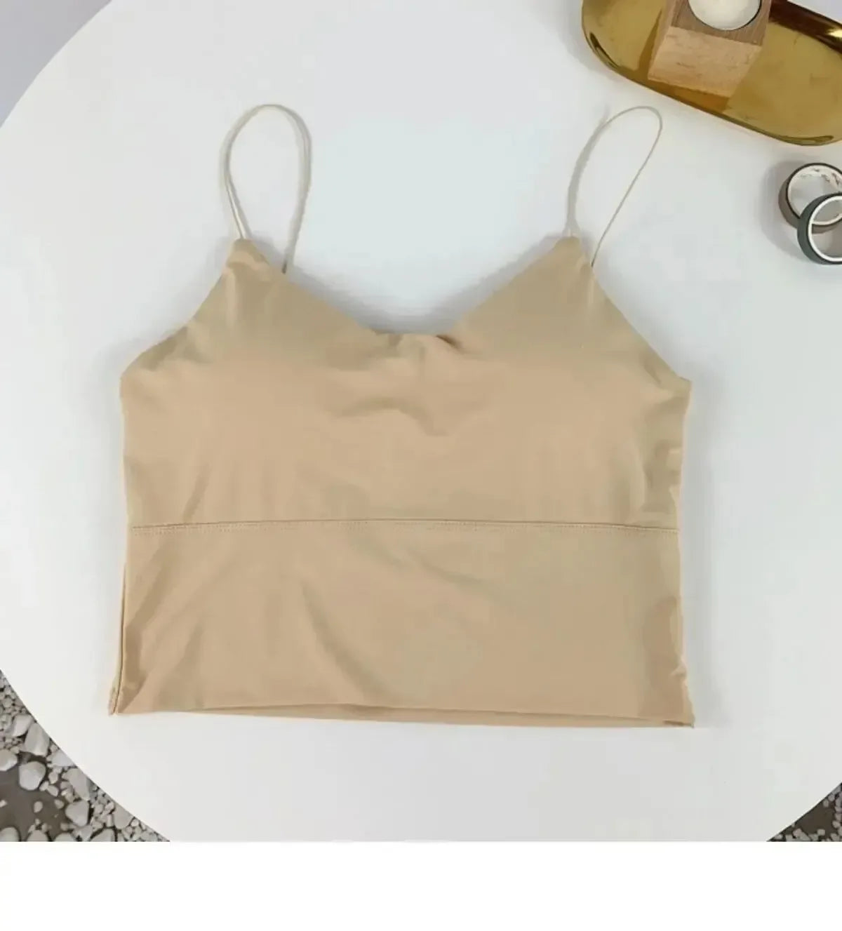 Beige crop top on a white surface with a gold object in the background