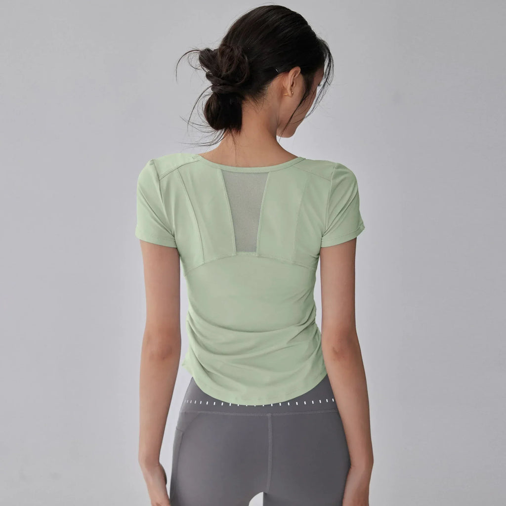 Woman wearing a light green athletic top and gray leggings on a gray background