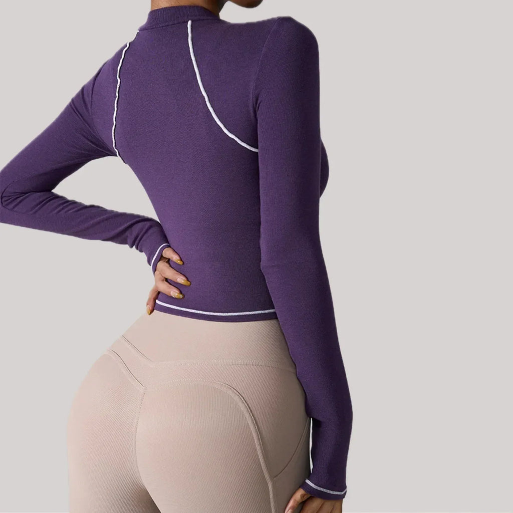 Person wearing a purple long-sleeve top and beige leggings on a gray background