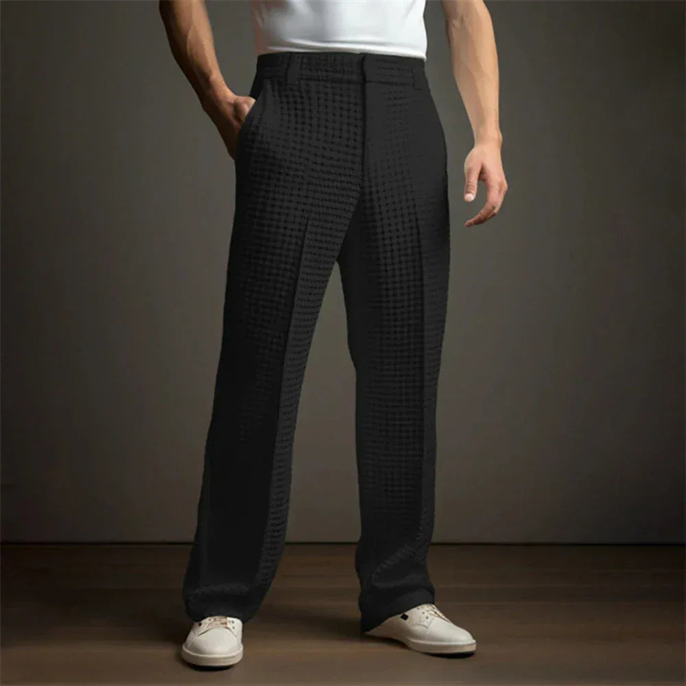 Person wearing black checkered pants and white shoes on a plain background