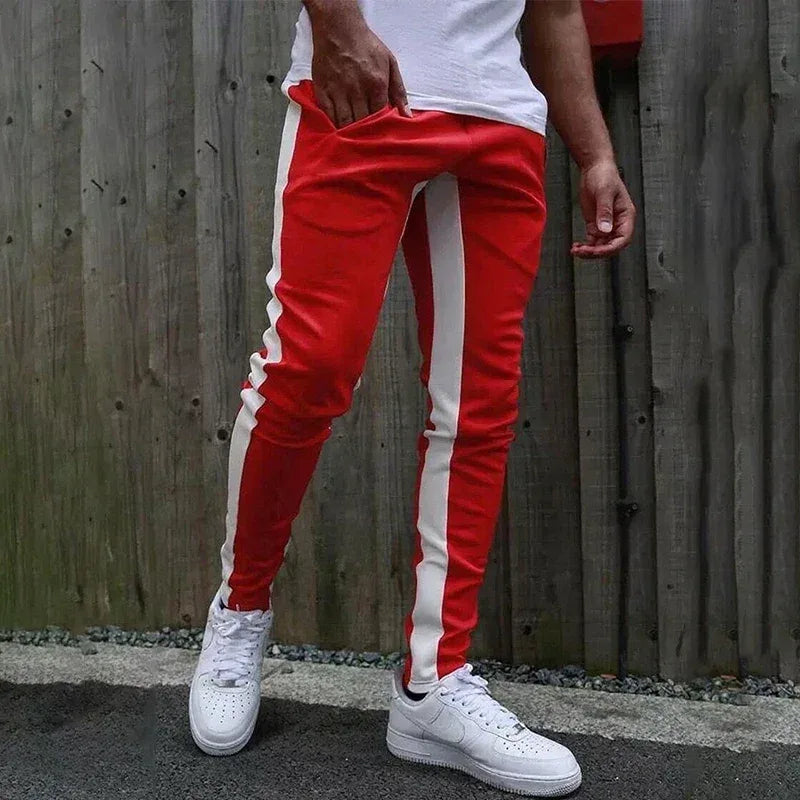 Person wearing red jogger pants with white stripes and white sneakers against a wooden fence background.