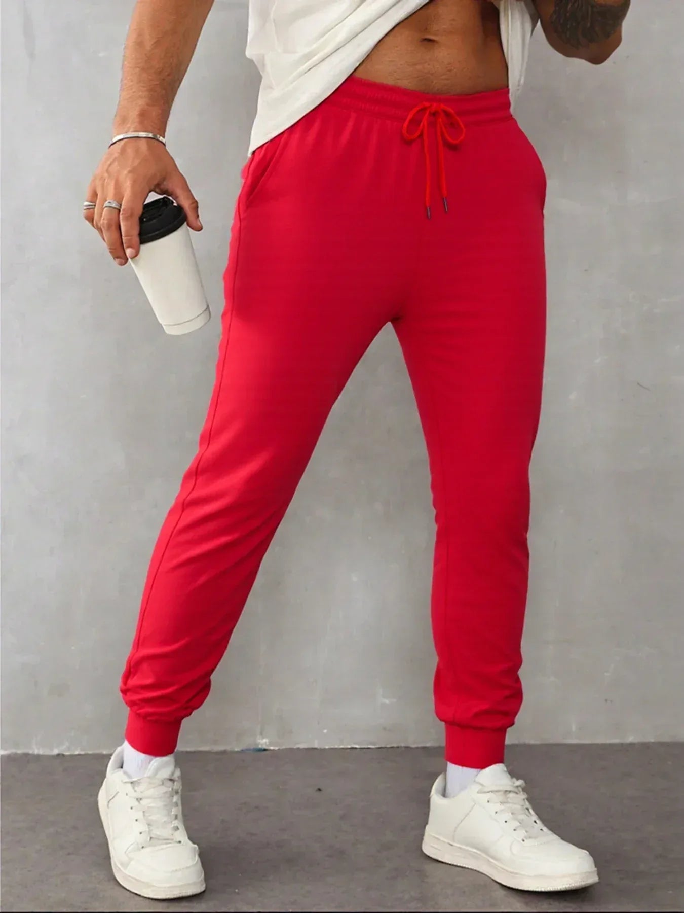 Person wearing red sweatpants and white sneakers against a gray background