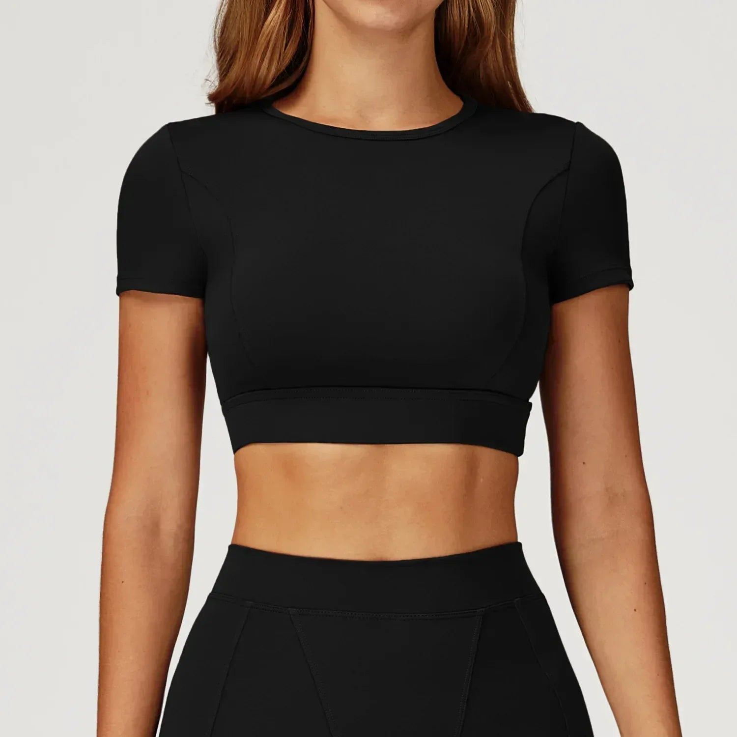 Person wearing a black crop top and black pants on a light gray background