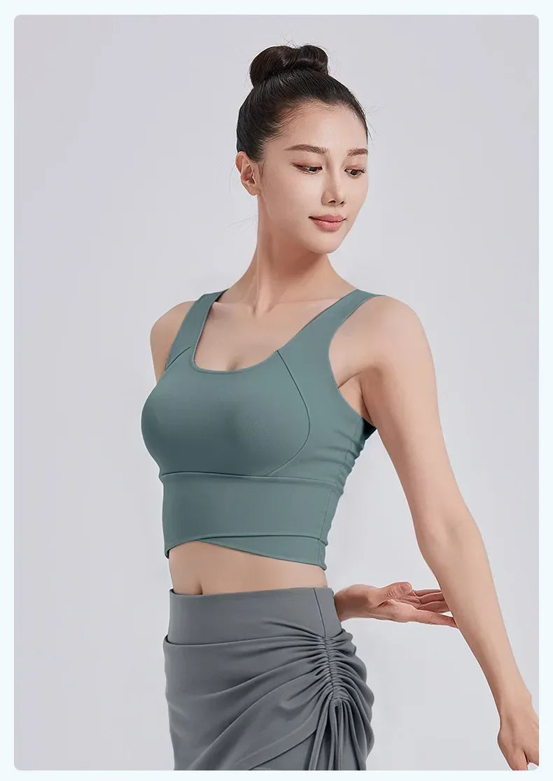 Woman wearing a green sports bra and gray leggings on a light gray background