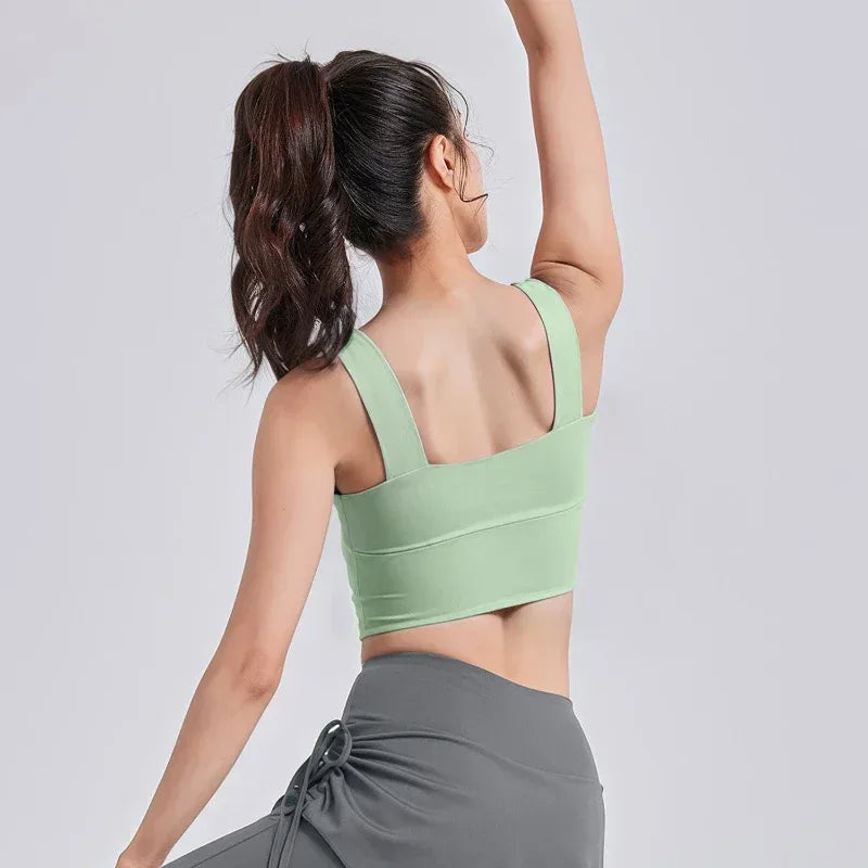 Woman wearing a green sports bra and gray pants on a white background