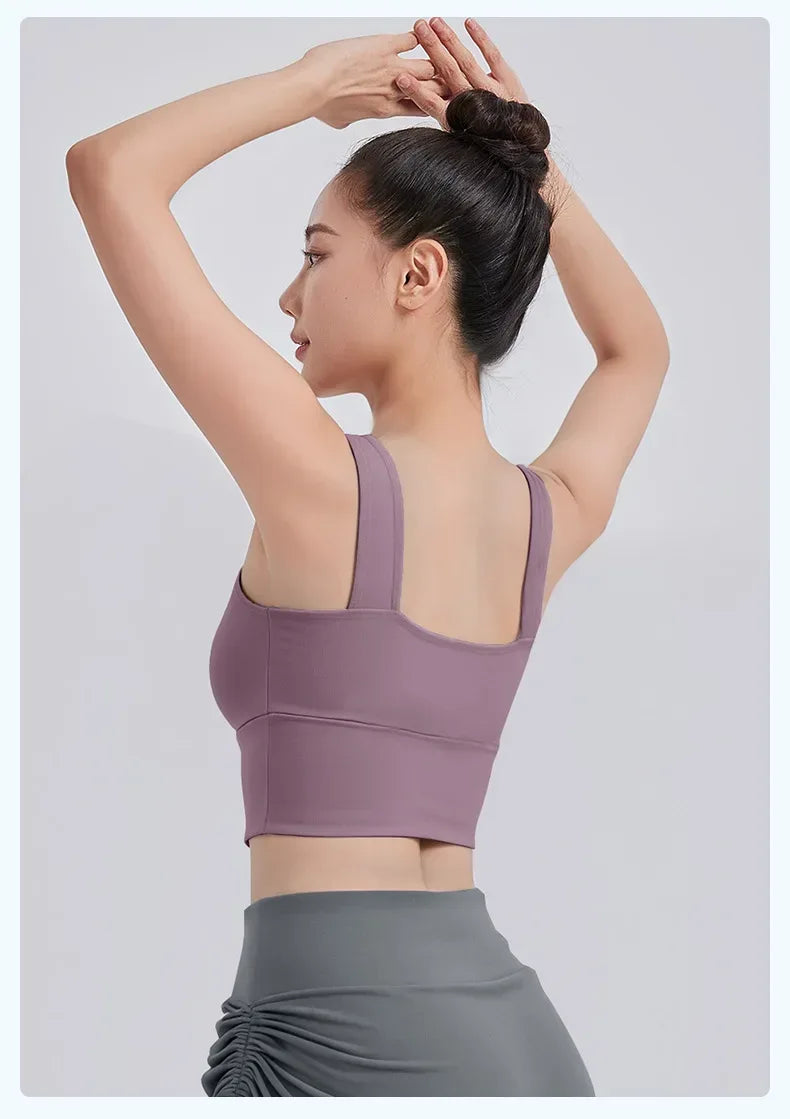 Woman wearing a purple sports bra and gray leggings on a light gray background