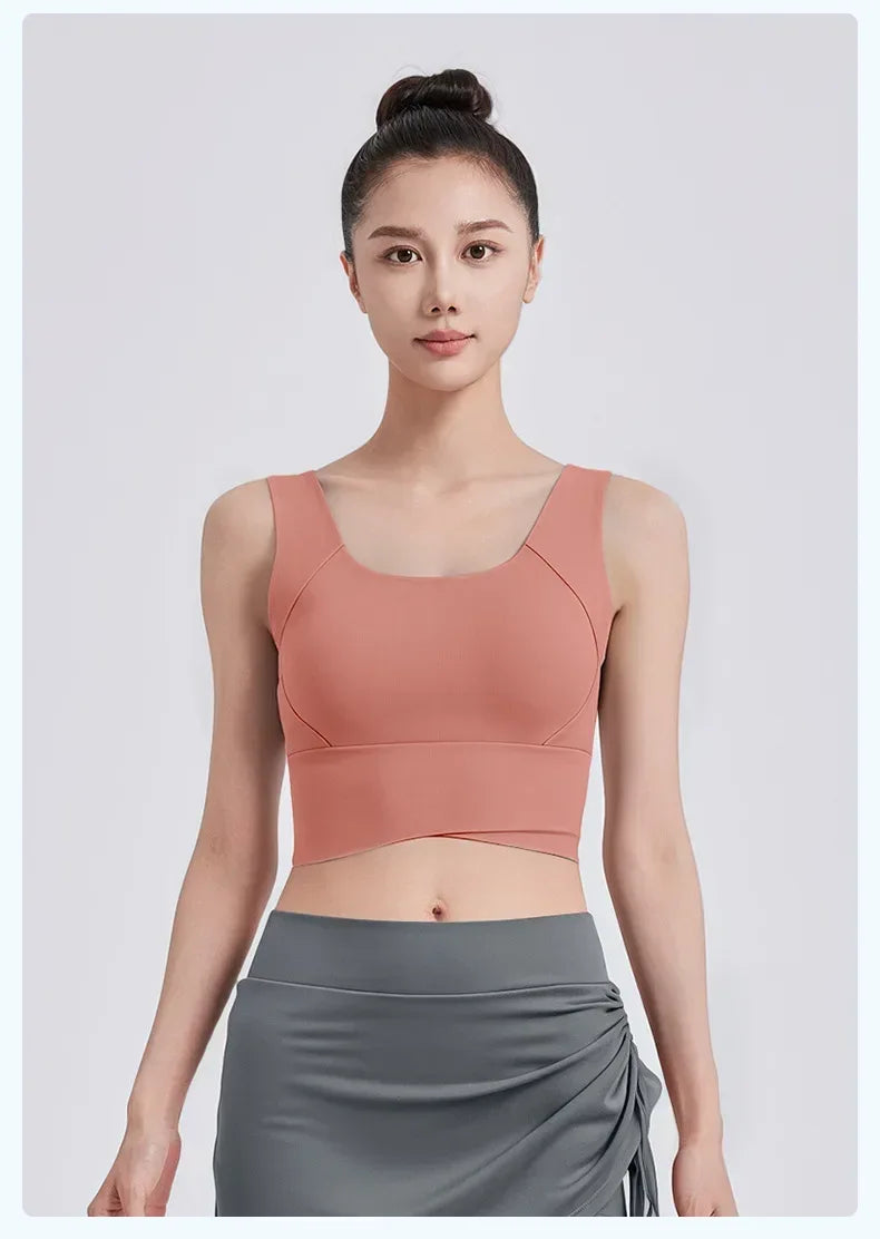 Woman wearing a peach-colored sports bra and gray leggings on a light gray background