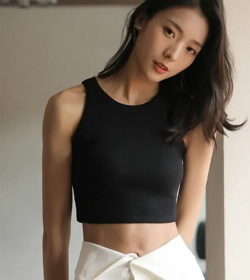 Woman wearing a black sleeveless top and white pants against a neutral background