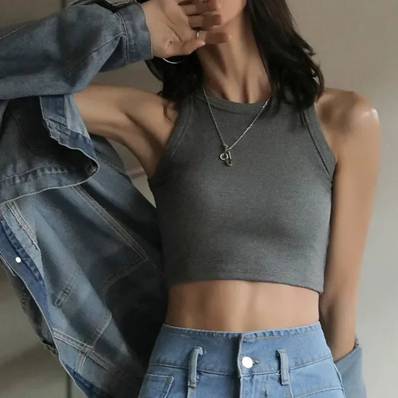 Person wearing a gray crop top and blue jeans with a blurred background