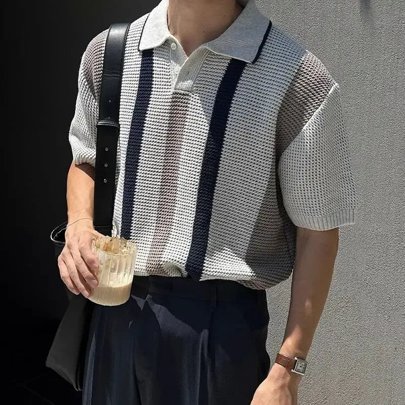 Person wearing a patterned shirt and suspenders, holding a drink against a gray background