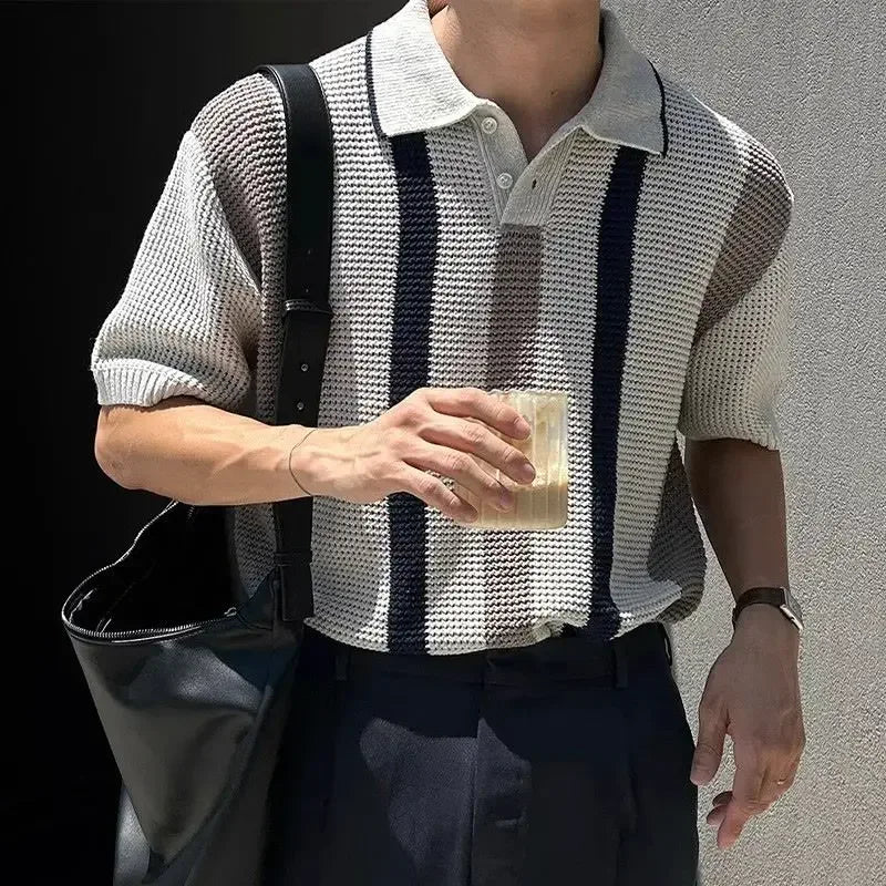 Person wearing a patterned shirt holding a drink against a gray background