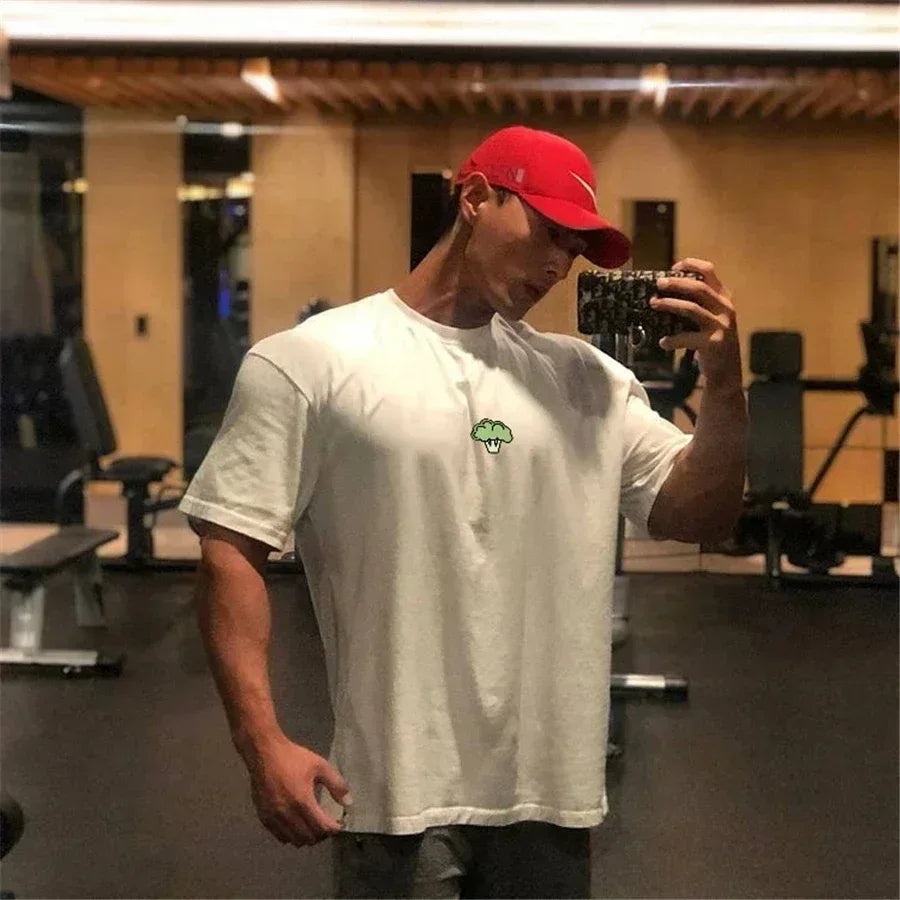 Person wearing a white t-shirt with a logo and a red cap in a gym setting.