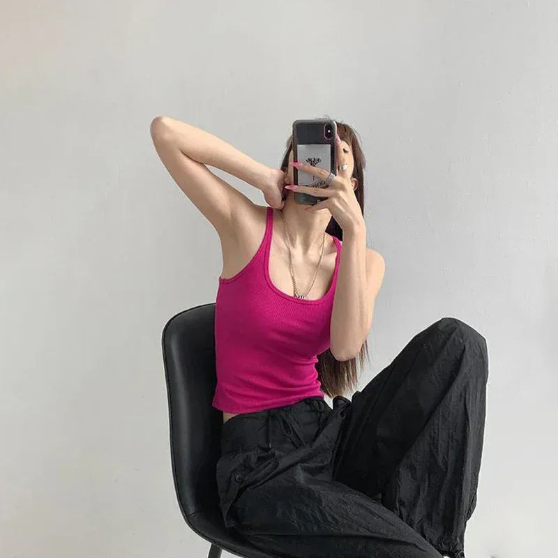 Person taking a mirror selfie wearing a pink tank top and black pants on a plain background