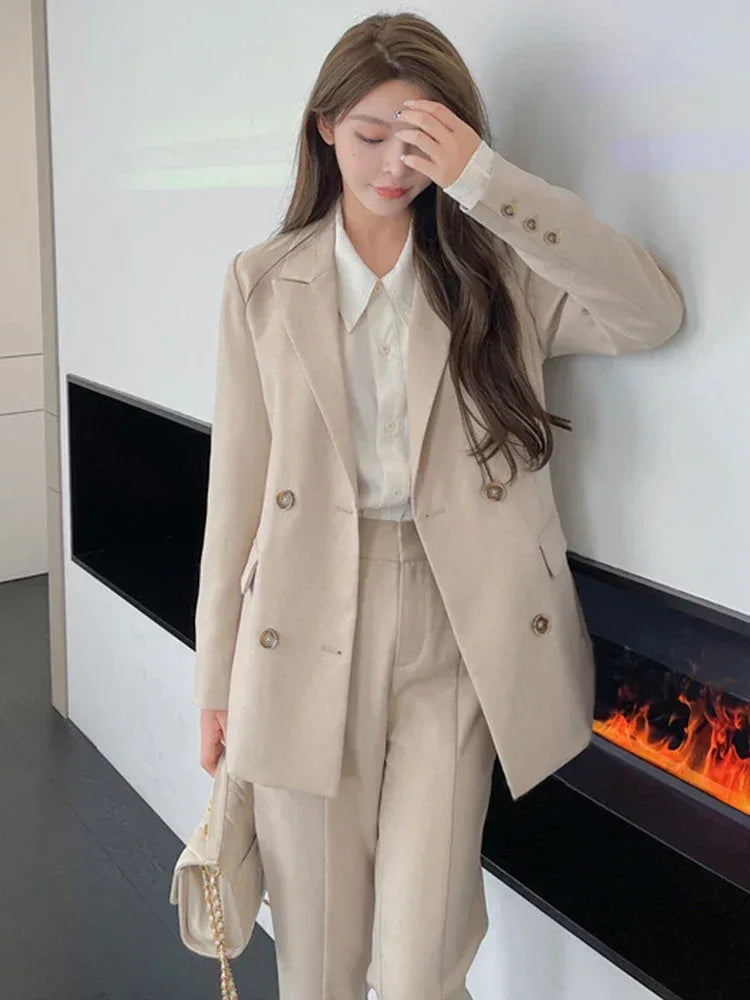 Woman wearing a beige suit in a modern room with a fireplace.
