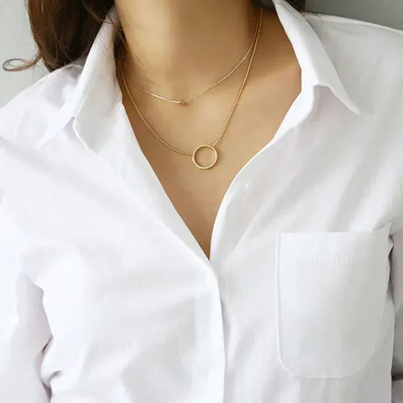 Gold necklace with a circular pendant on a white shirt