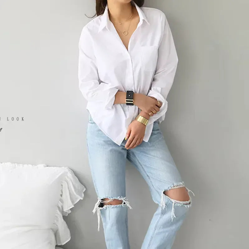 Person wearing a white shirt and light blue ripped jeans against a gray background