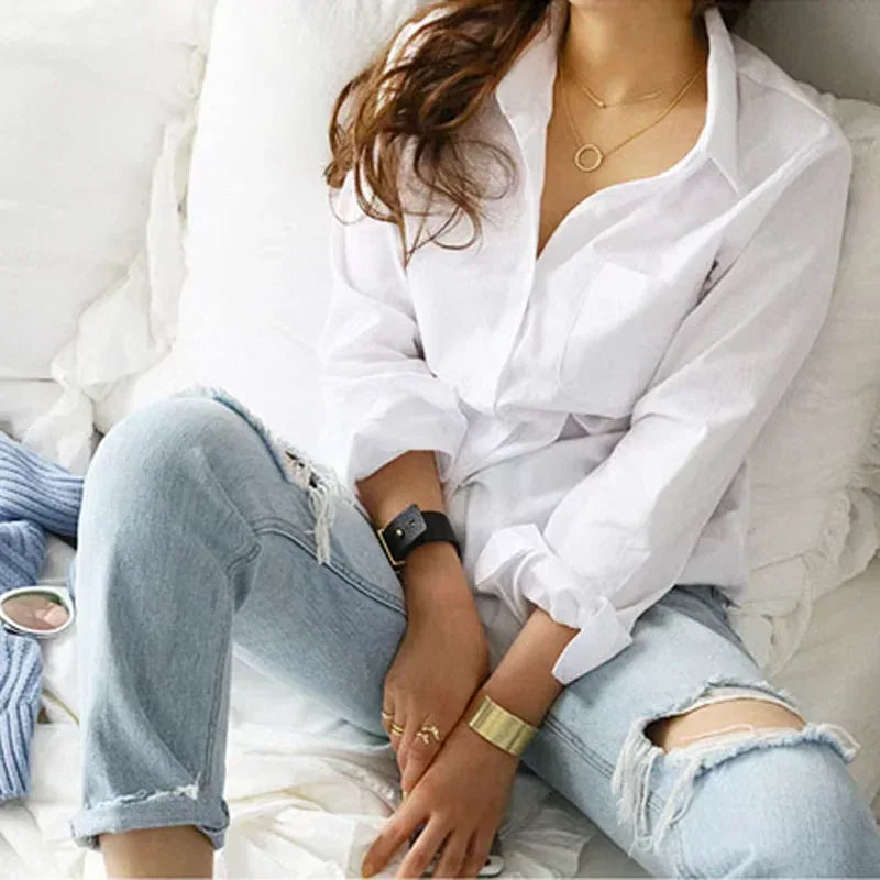 Person wearing a white shirt and light blue jeans sitting on a bed.