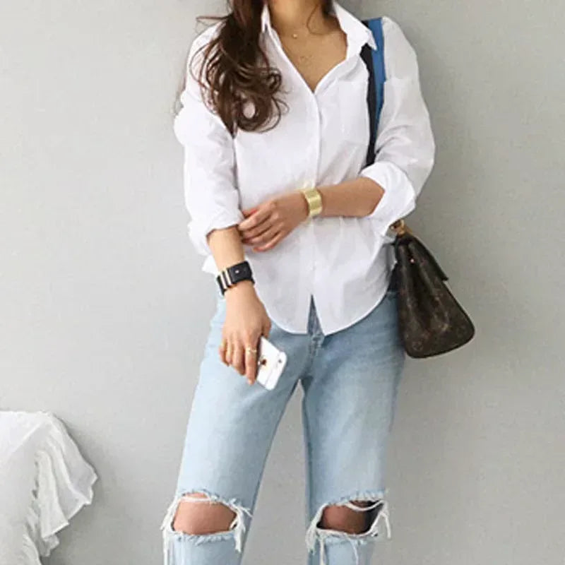 Person wearing a white shirt and light blue jeans with a brown handbag on a plain background