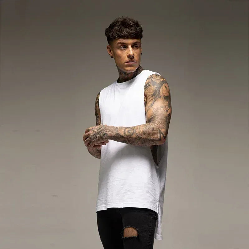 Man wearing a white sleeveless shirt with tattoos on arms against a gray background