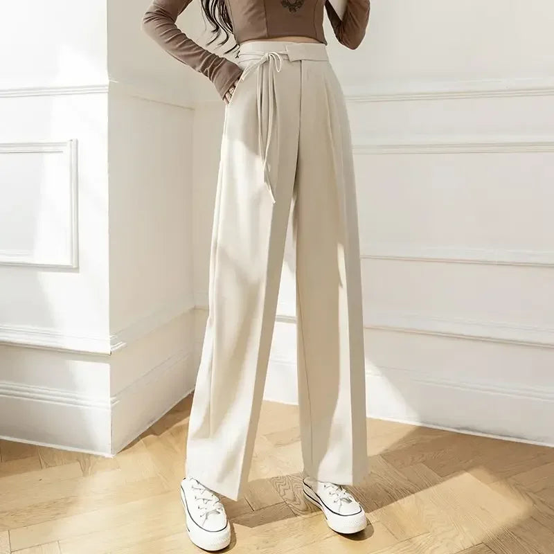 Person wearing beige wide-leg pants and a brown top in a room with white walls and wooden floor.