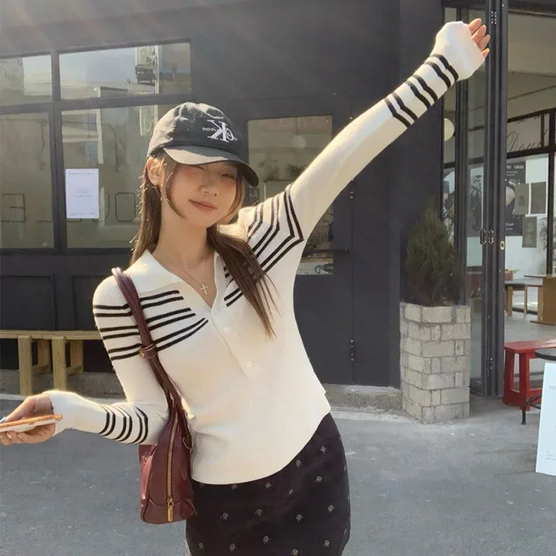 Woman wearing a white sweater with black stripes, dark cap, and polka dot skirt outdoors.