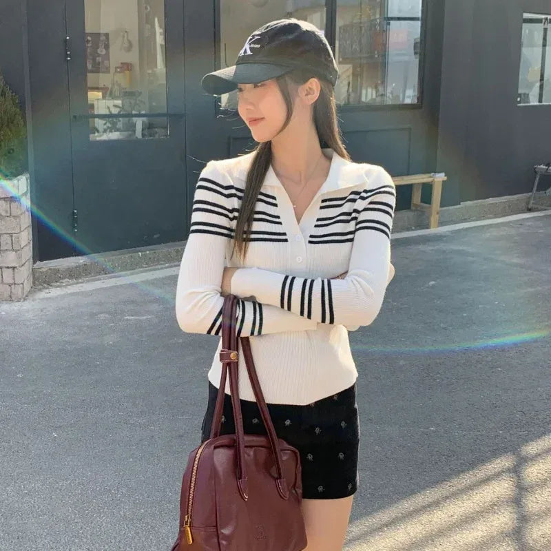 Woman wearing a striped sweater and cap, holding a brown bag on a street.