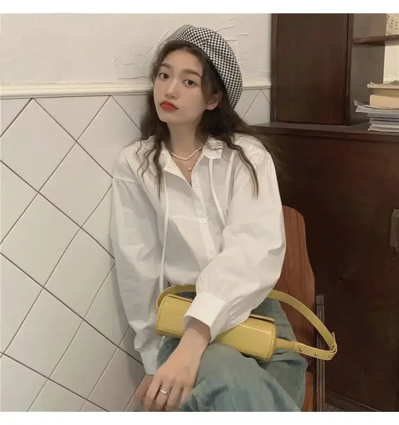 Woman wearing a white shirt and checkered beret, holding a yellow bag in a tiled room.