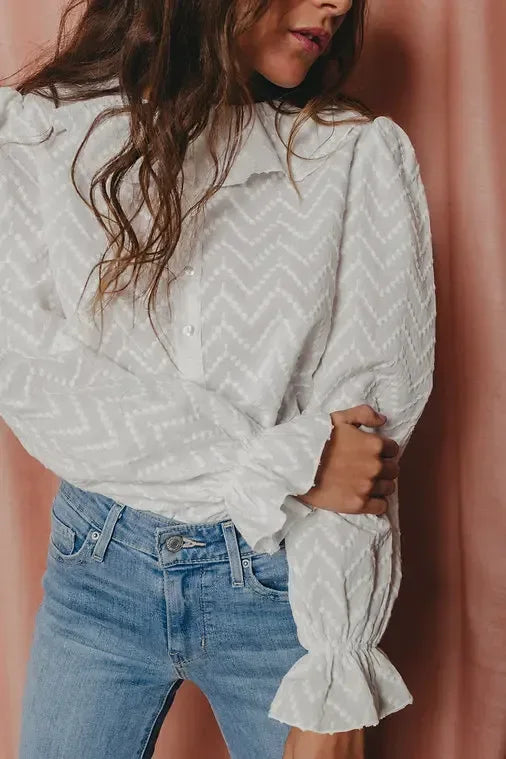 Person wearing a white patterned blouse and blue jeans against a pink background