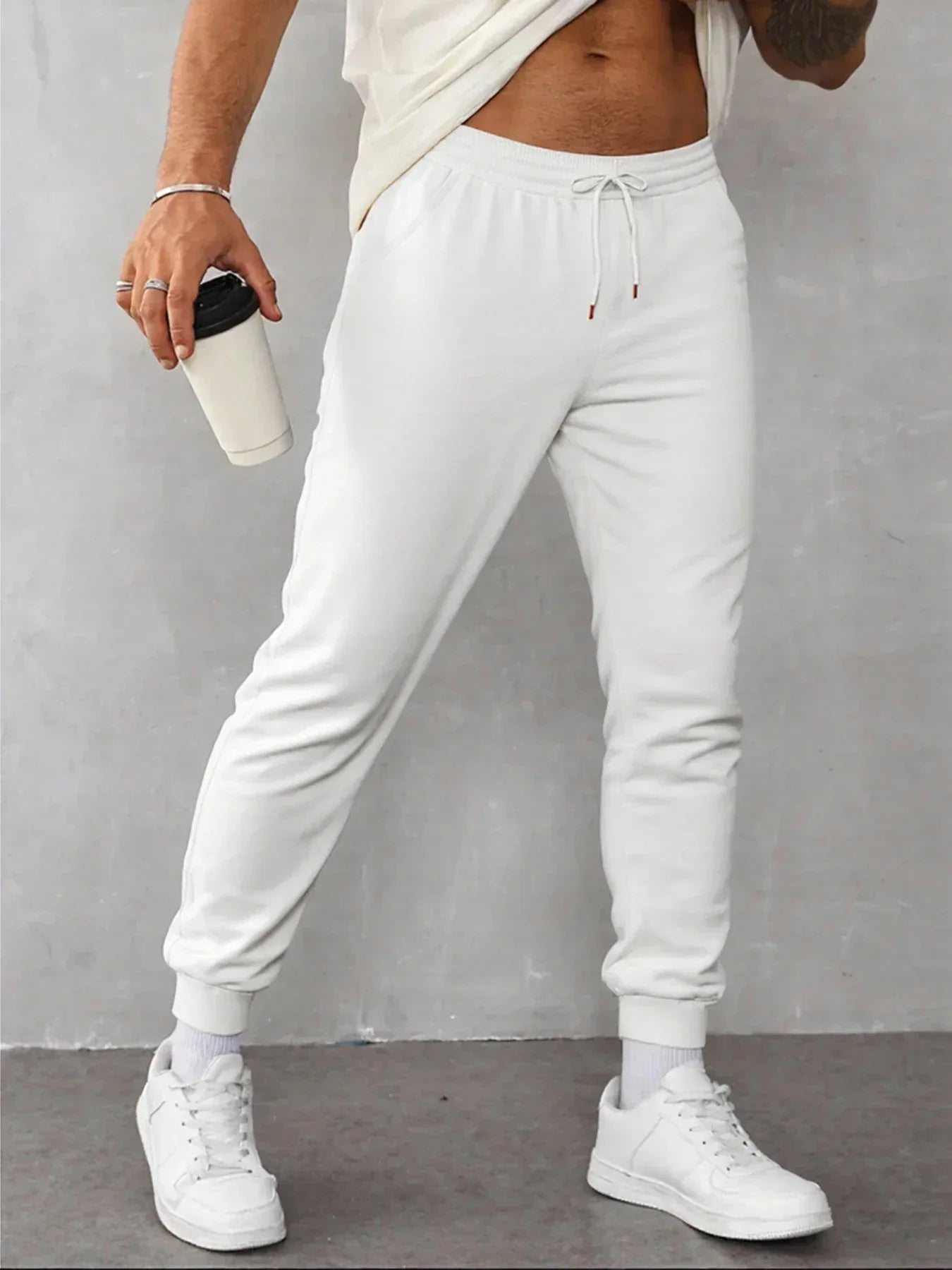 Person wearing white sweatpants and white sneakers against a gray background
