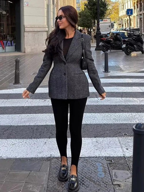 Woman in a gray blazer and black pants crossing a zebra crossing in an urban setting.