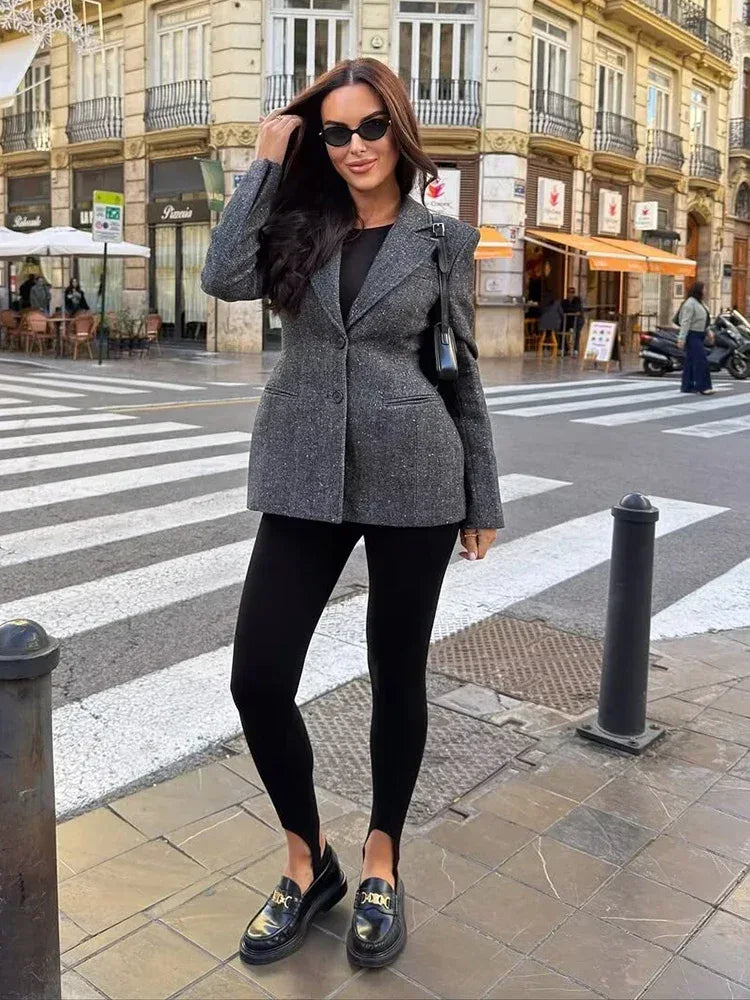 Woman in a gray blazer and black leggings standing on a city street.